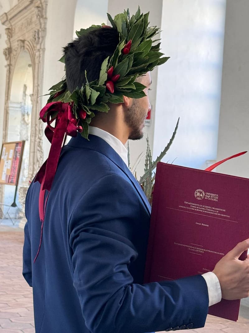Foto di Omar di spalle con corona di alloro e titolo della tesi di laurea sui database repertoriali, con copertina rossa